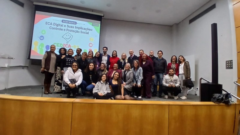 Grupo de pessoas em cima do palco, com painel sobre o ECA Digital ao fundo